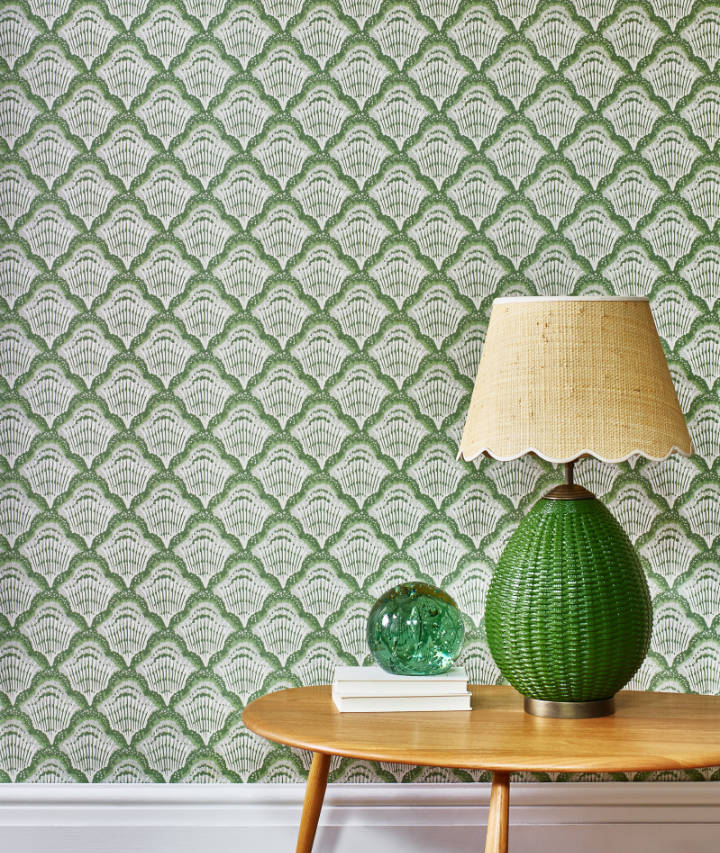 A small side table with a green lamp in front of a green pattern wallpapered wall